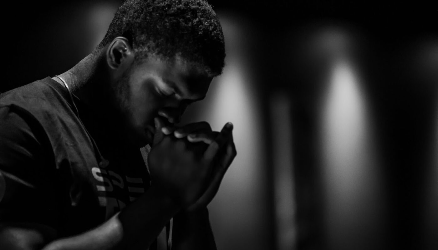 Homme les yeux fermés, les mains jointes devant son visage dans un environnement sombre