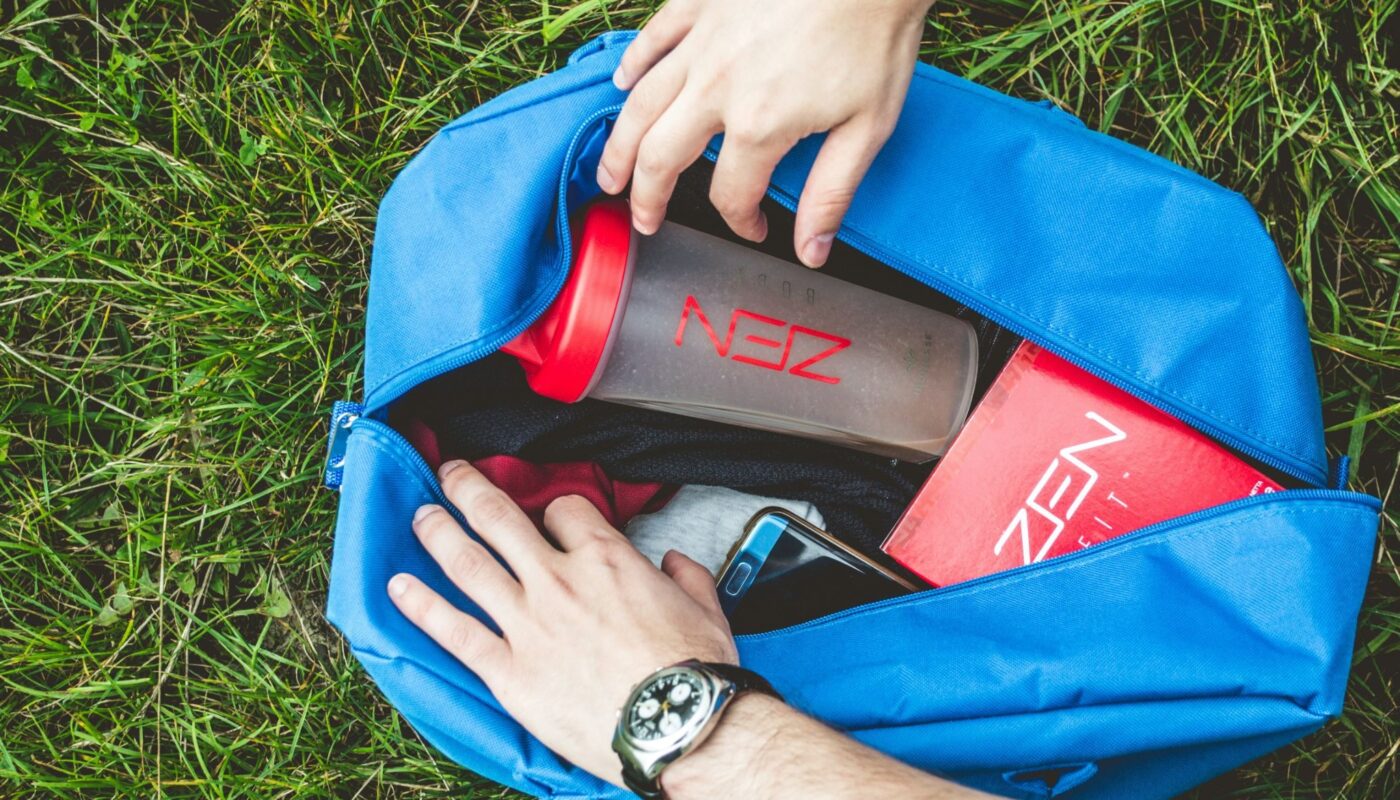 Sac de sport ouvert posé sur l’herbe contenant une gourde, un téléphone et des vêtements