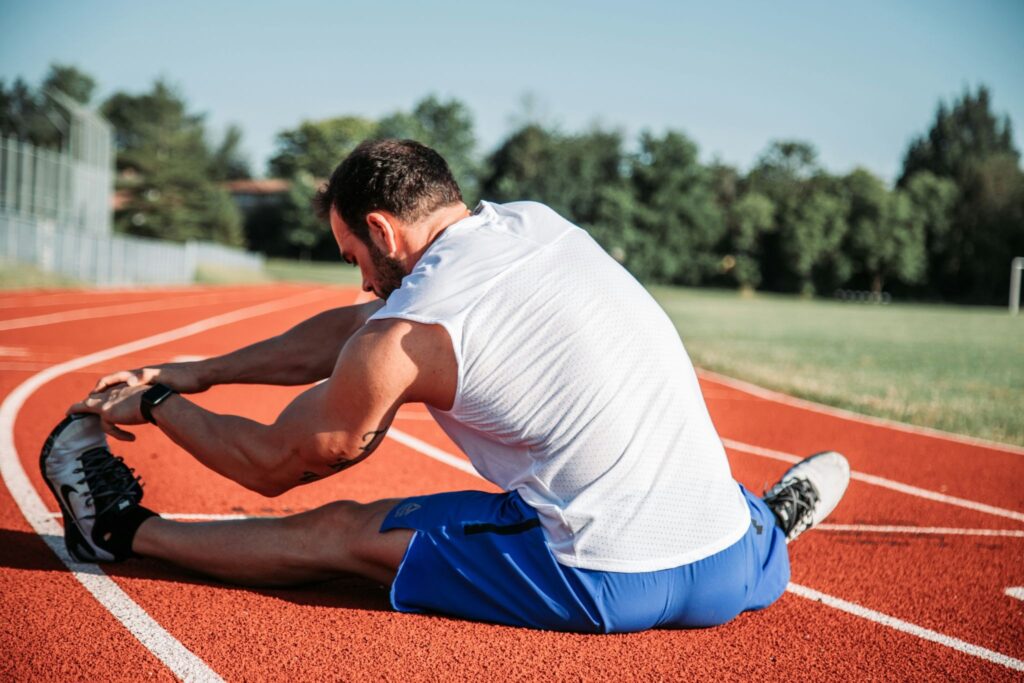 Athlète assis sur une piste d’athlétisme en train de s’étirer après un entraînement