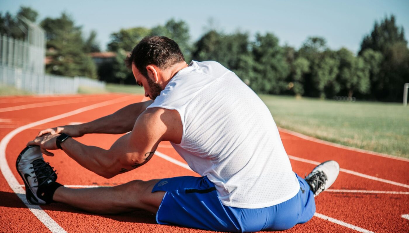 Athlète assis sur une piste d’athlétisme en train de s’étirer après un entraînement