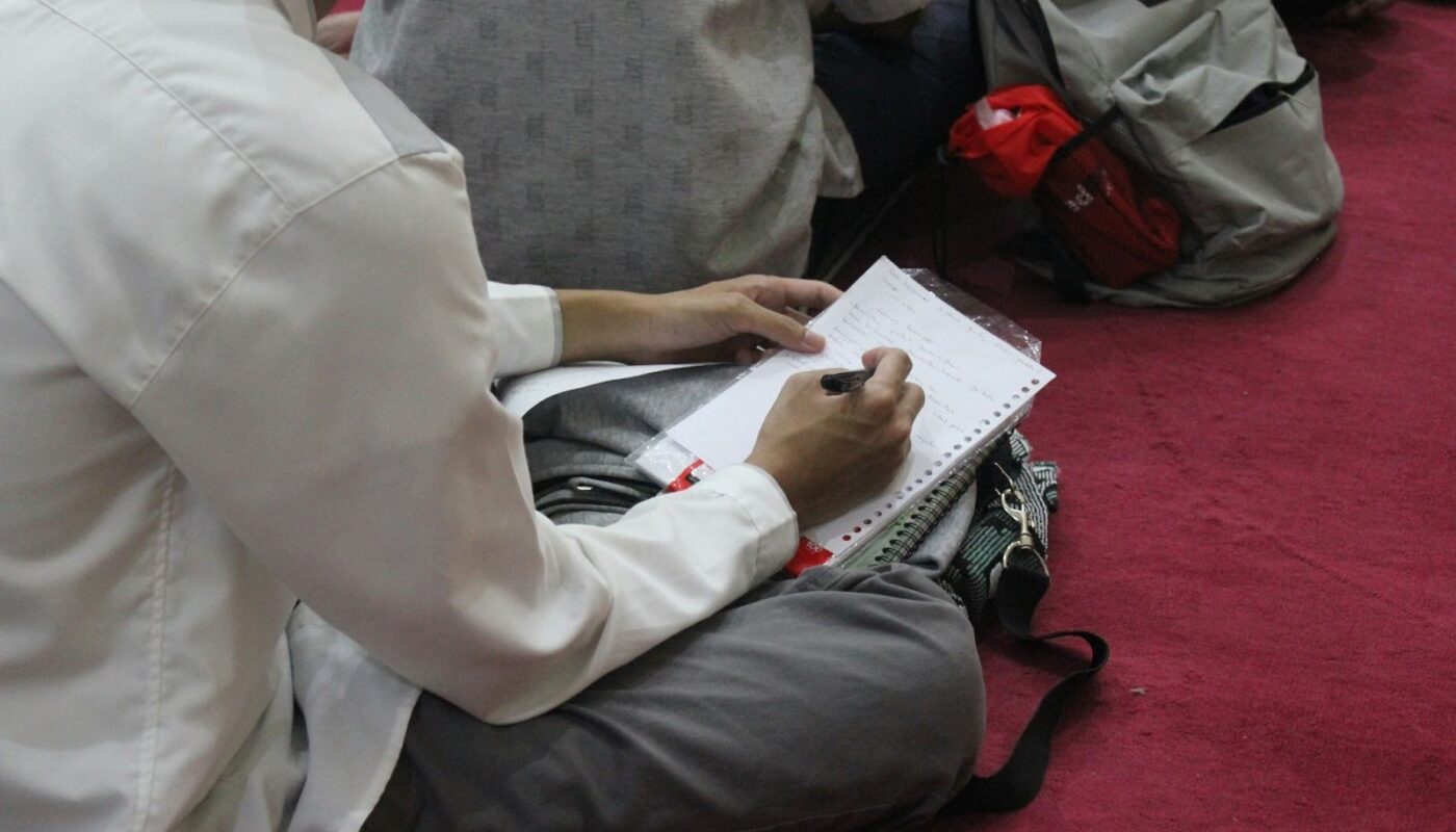 Personne assise prenant des notes sur une feuille de papier, avec un sac posé à côté