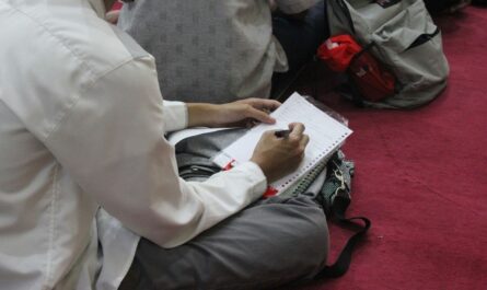 Personne assise prenant des notes sur une feuille de papier, avec un sac posé à côté