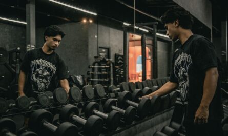 Homme debout dans une salle de sport, regardant des haltères devant un miroir