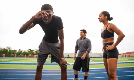 Trois personnes en tenue de sport sur une piste d’athlétisme, dont un homme penché vers l’avant