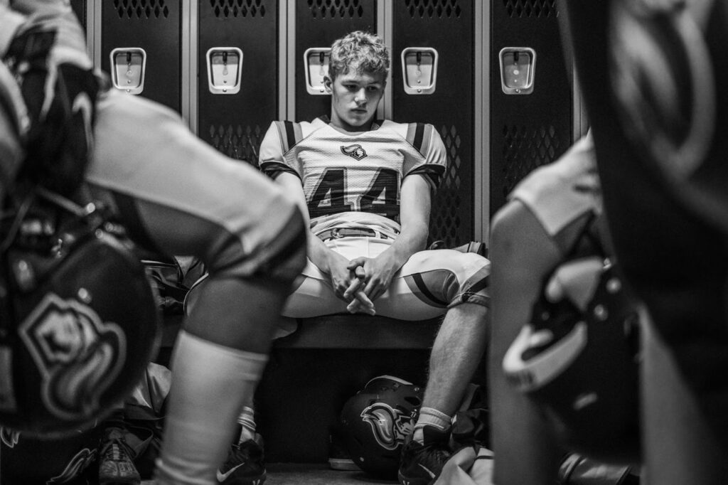 Joueur de football américain assis dans un vestiaire, entouré de ses coéquipiers