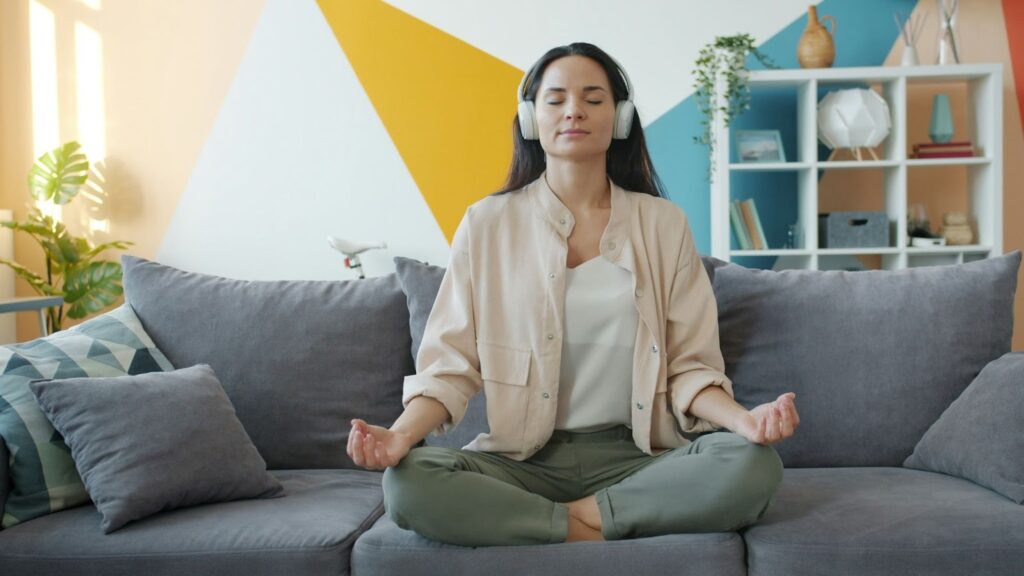 Femme assise en tailleur sur un canapé, portant un casque audio et gardant les yeux fermés