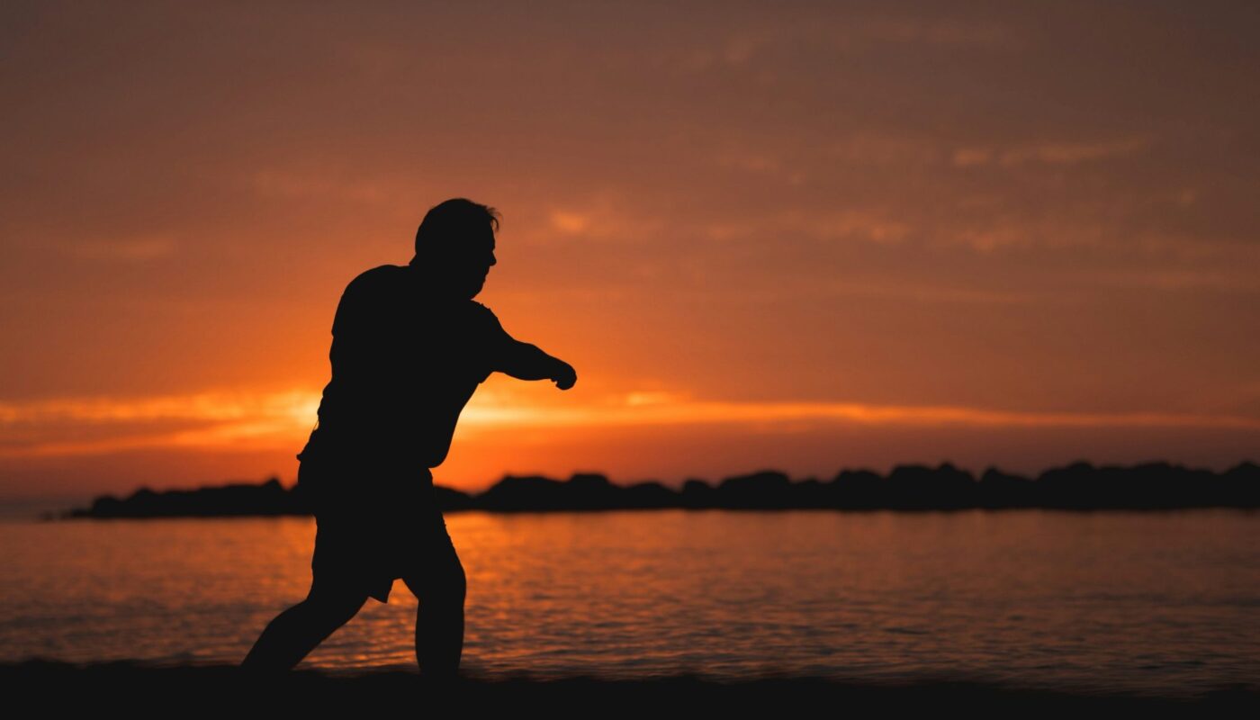 Silhouette d’un homme marchant au bord de l’eau au coucher du soleil
